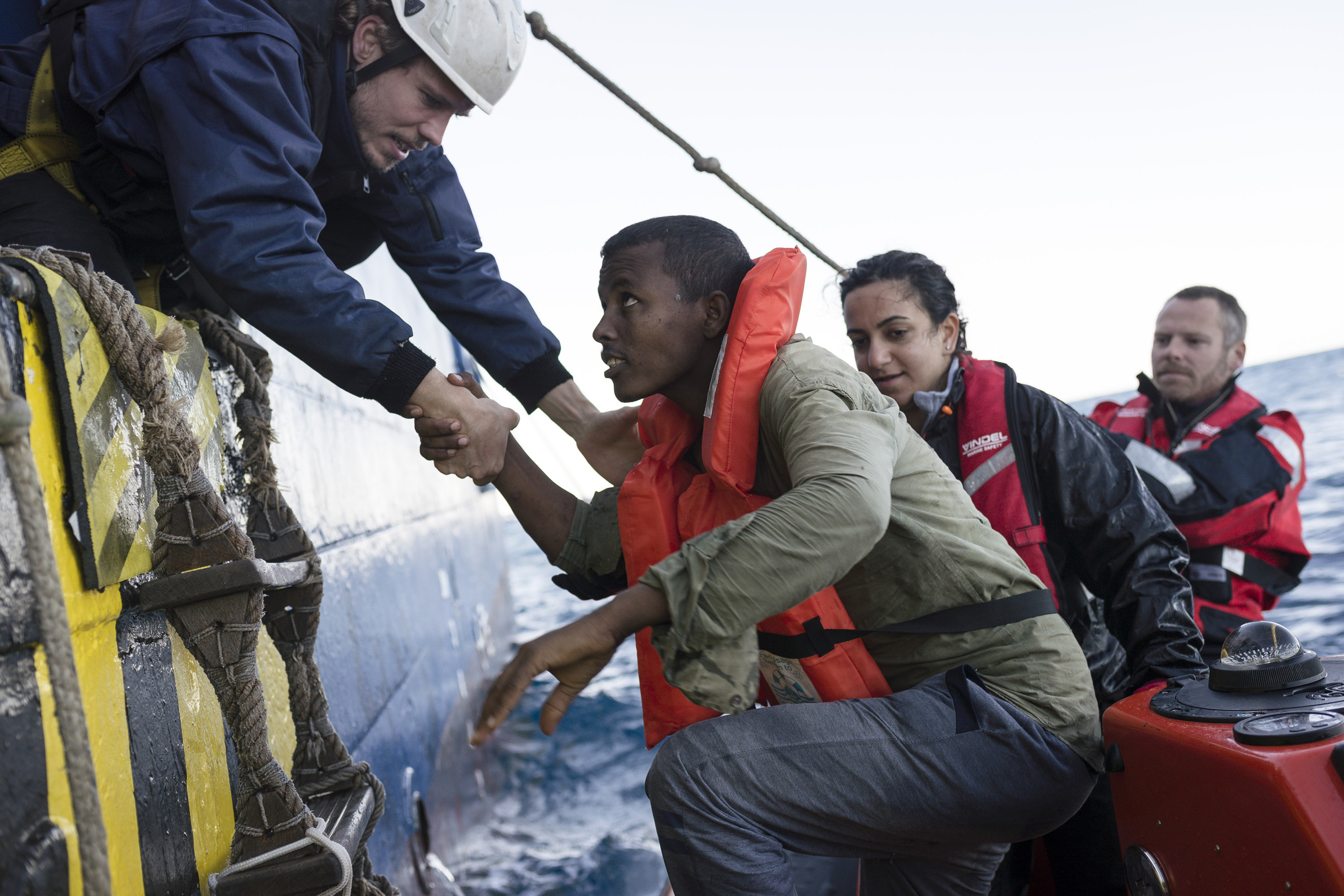 A rescue team help a migrant board their ship while at sea.