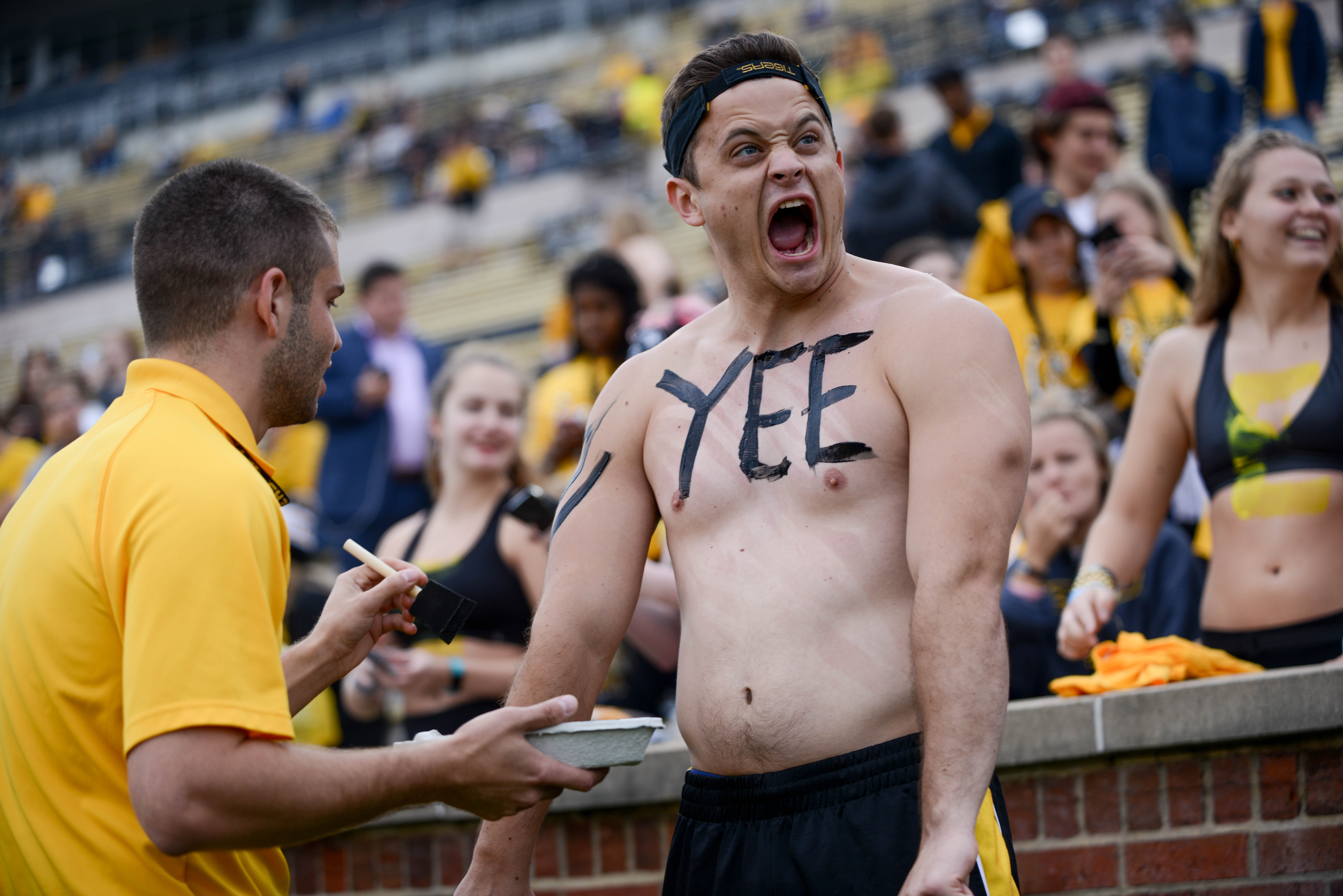 A Mizzou fan stands with his shirt off as his body painted with lettering.