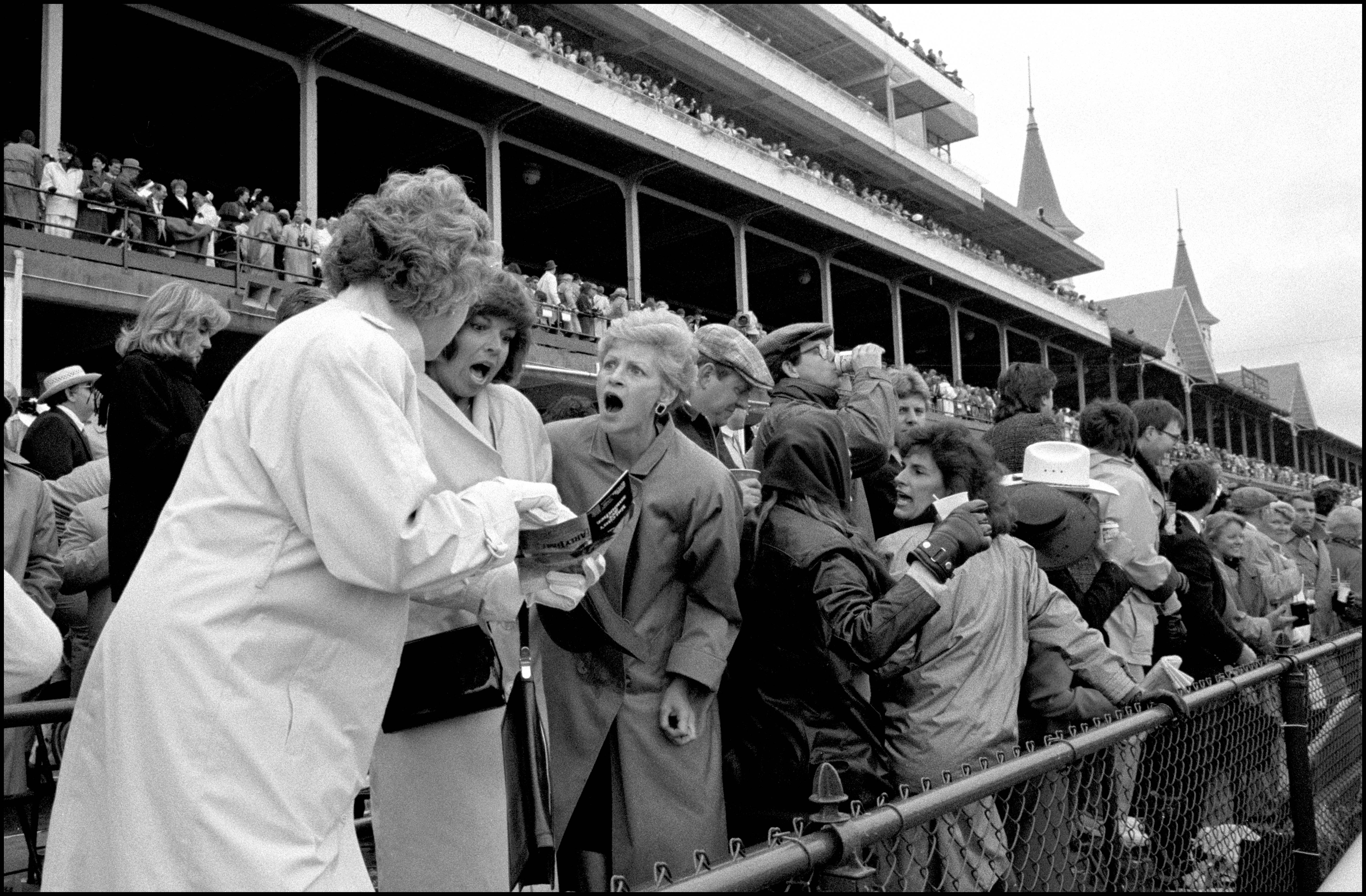 People stand against the railing at a horse race.