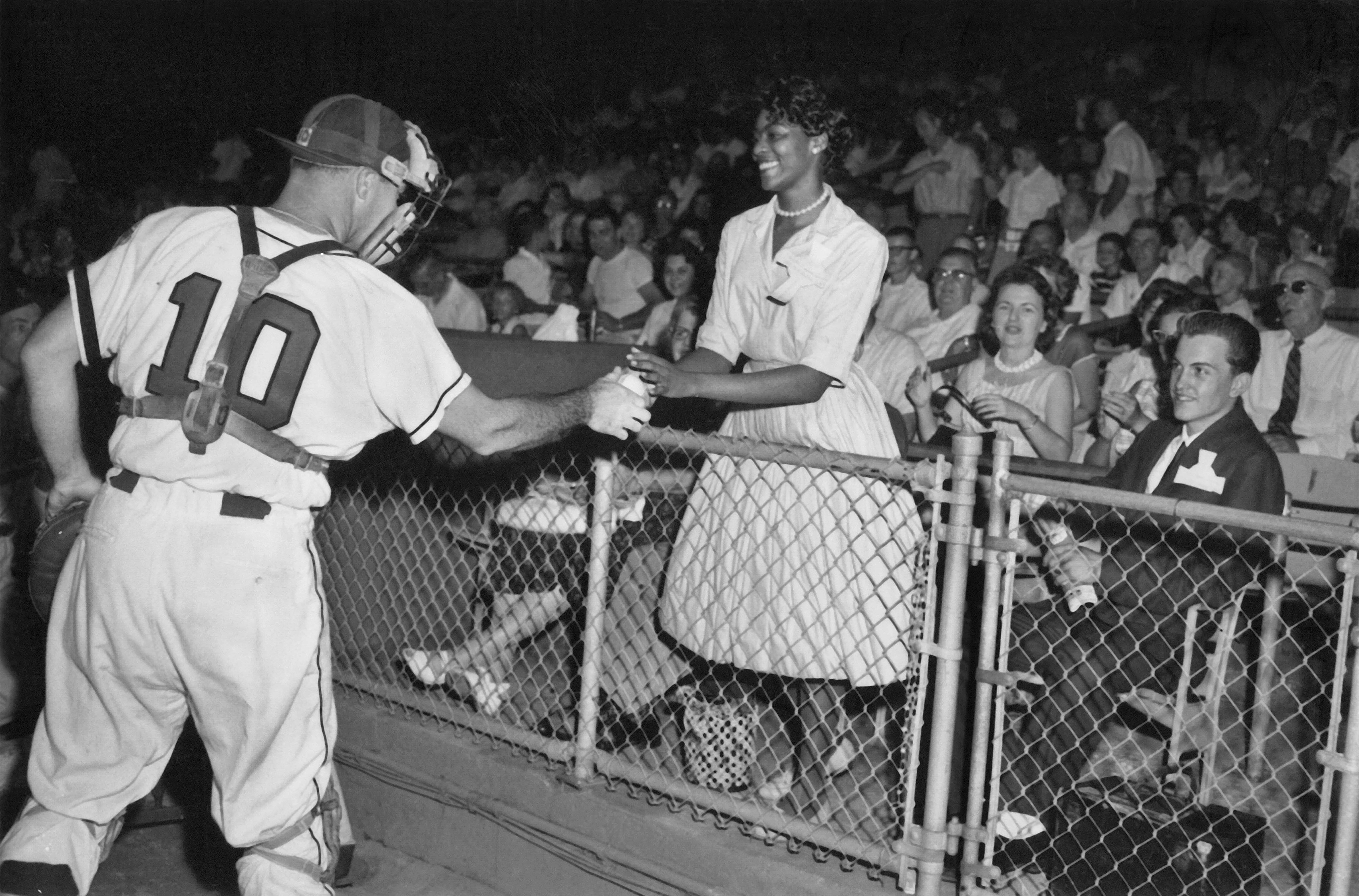 A catcher hands a baseball to a woman in the stands.