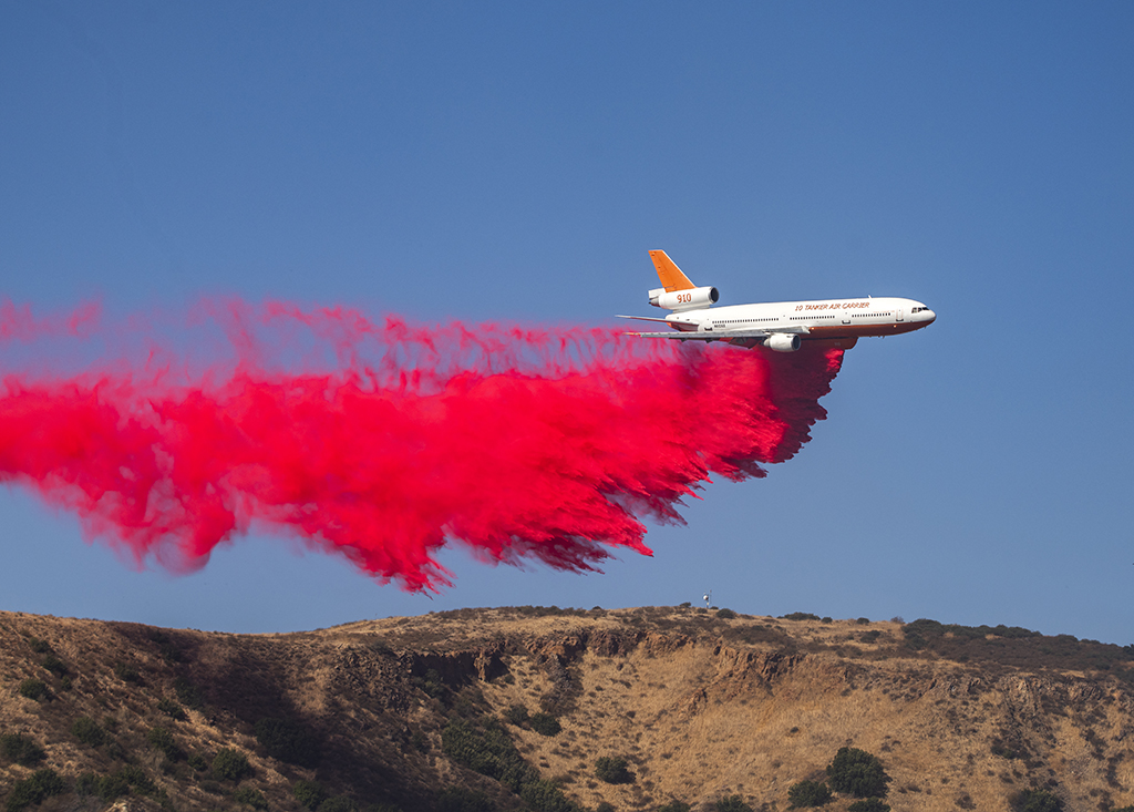 A large plan coats the ground with fire retardant chemicals as it flies over.