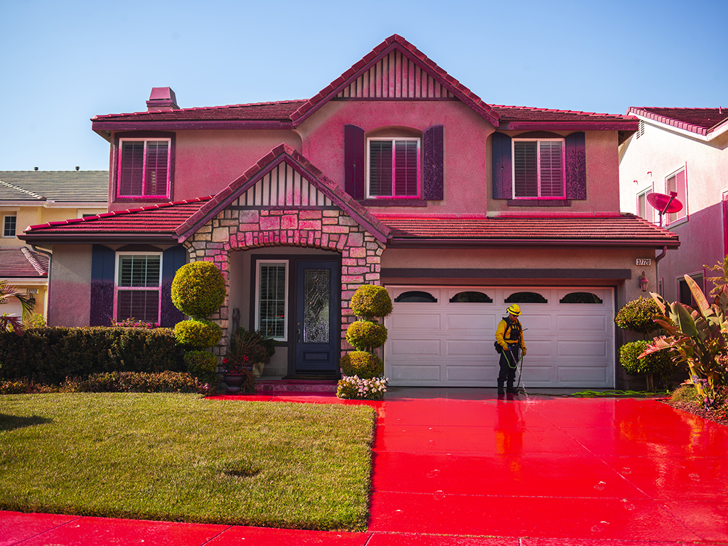 A fire fighter uses water to spray off the drive way of a house that was covered by red fire retardant chemicals.