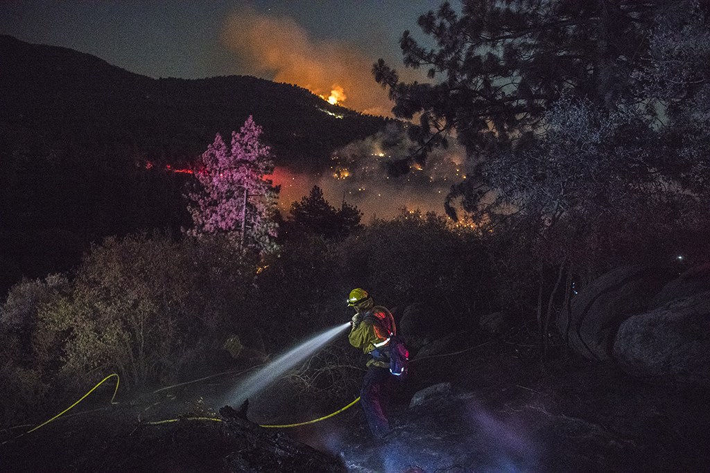 A fire fighter uses a fire house as fires spot the hillside in the distance.