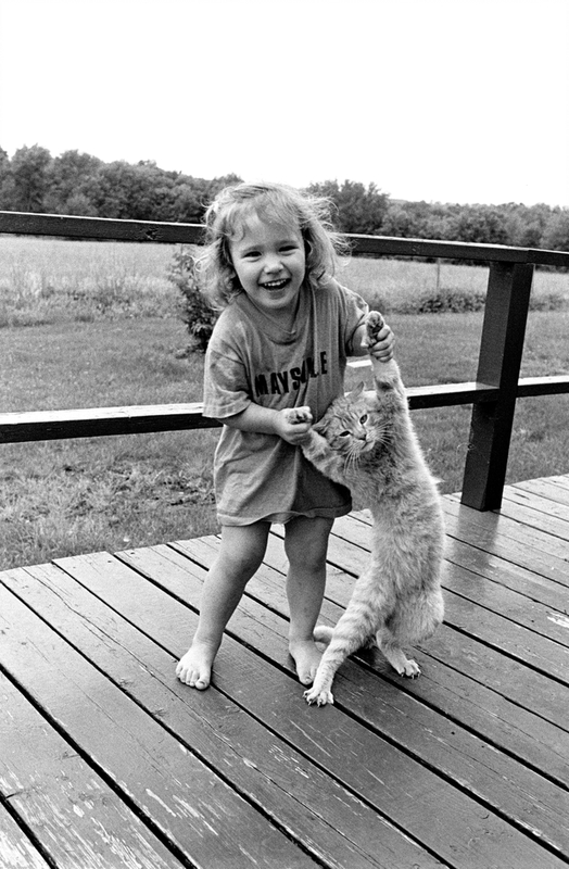 A young child stands a cat up on its rear legs.