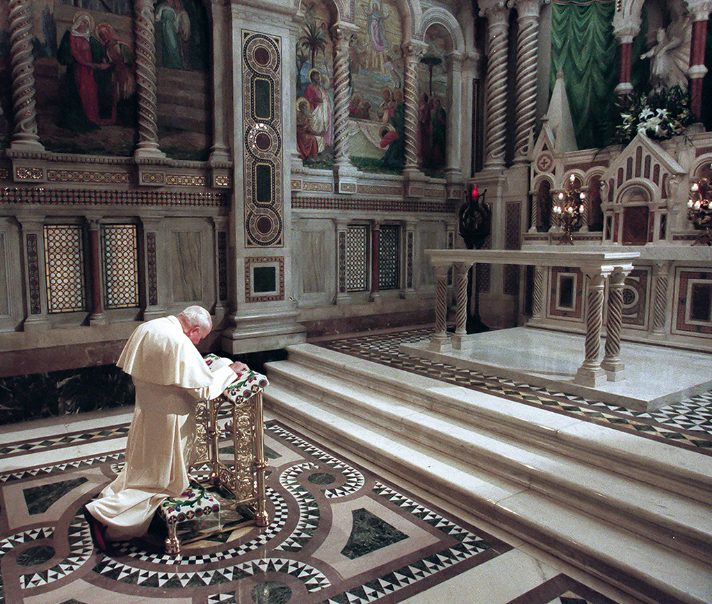 A catholic priest or religious leader kneels before an alter in a church.