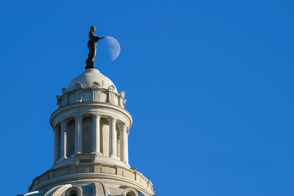 A statue atop a large structure is position to appear as if it is holding the moon. 