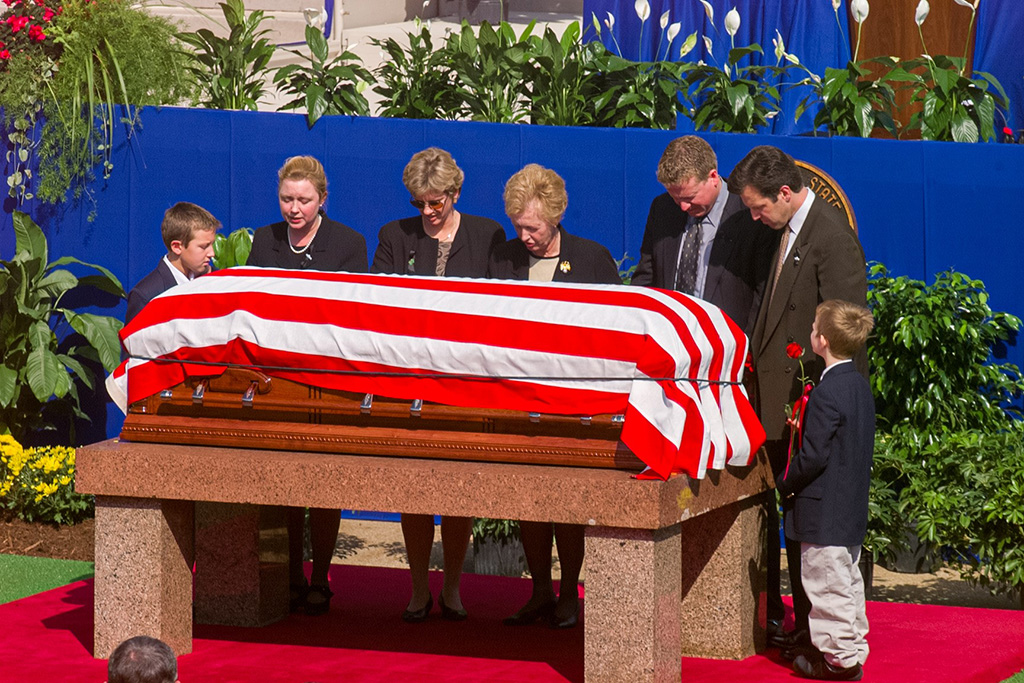 A family stands in mourning around a coffin draped with the American flag.