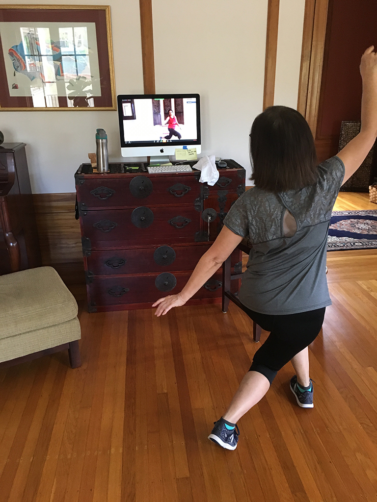 A woman follows along with a work out program projected on her computer while at home
