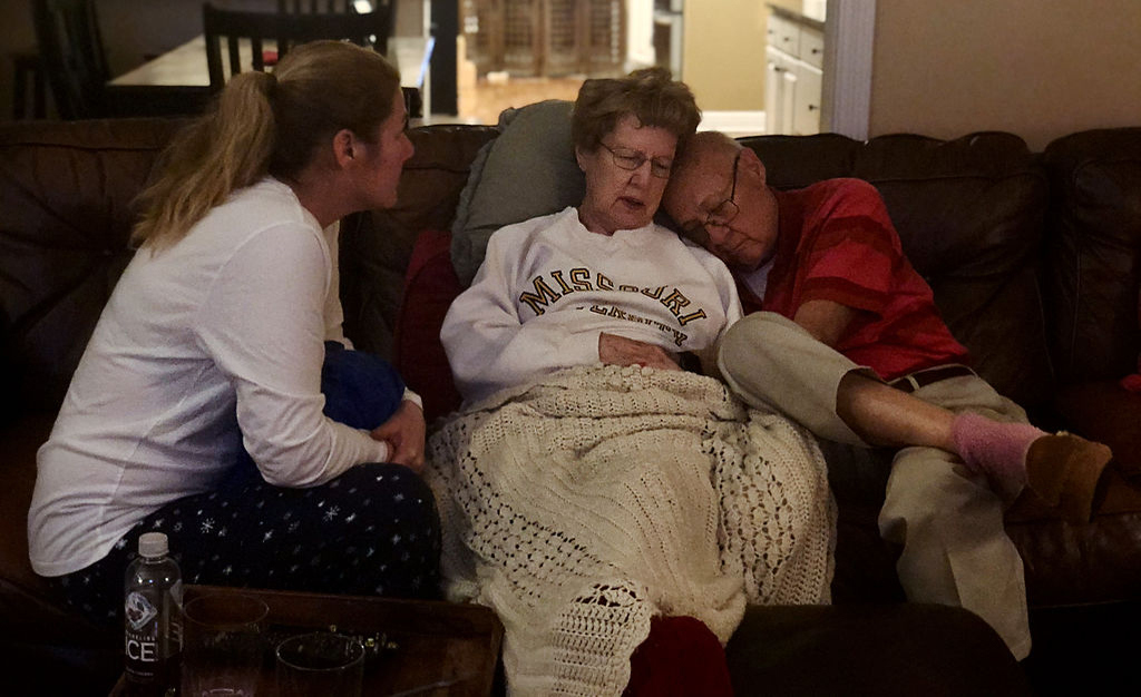 An elderly couple sit together on a couch next to a woman that could be their daughter.