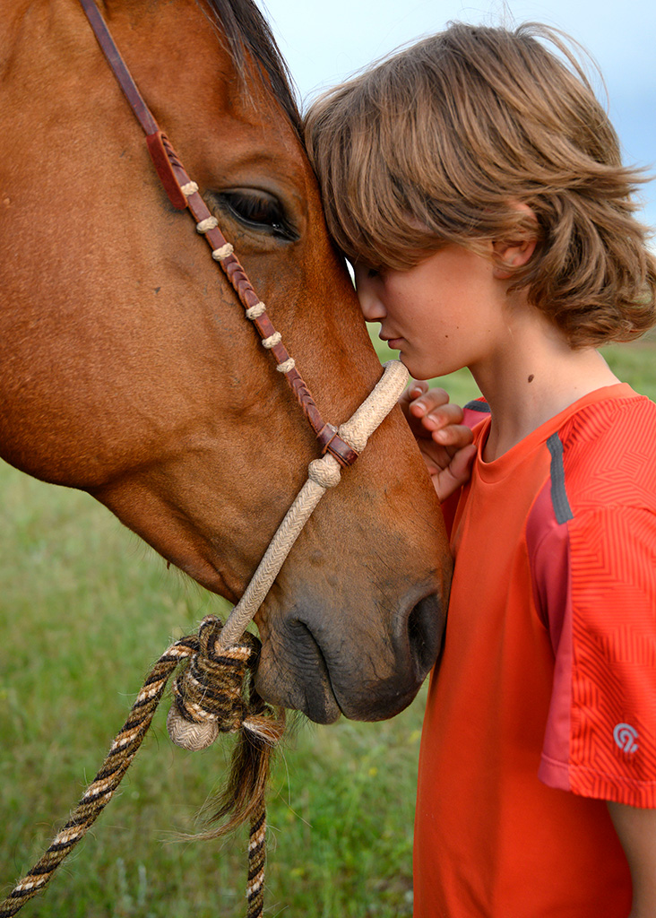 Photograph of a boy nuzzling a horse in Montana