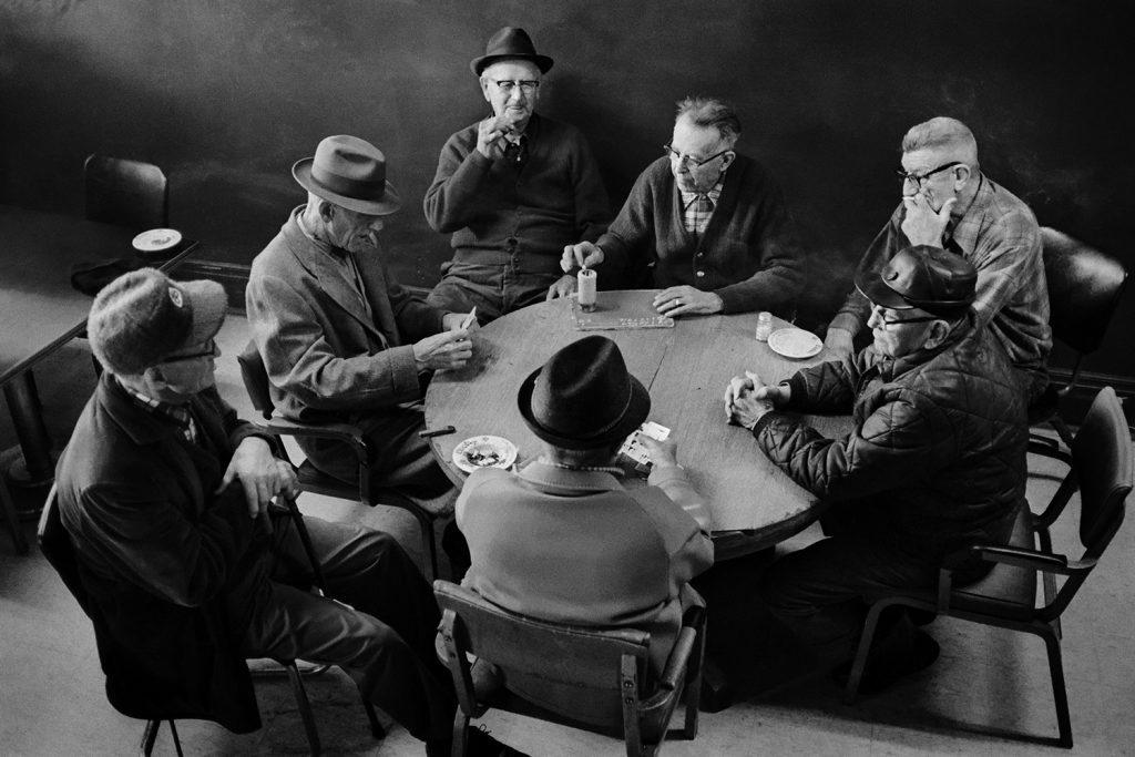 Elderly men sit around a table playing cards.