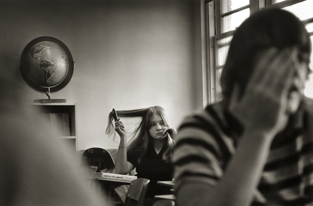 A high school student runs a comb through her hair while sitting in a classroom.