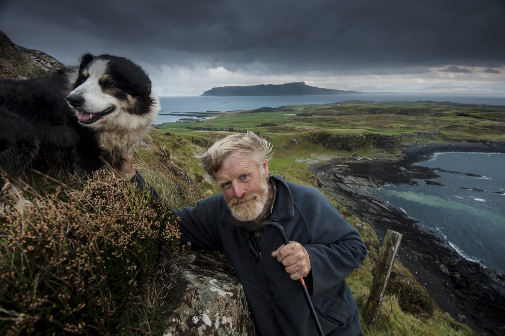 Man and a dog stands in front of a scenic background.