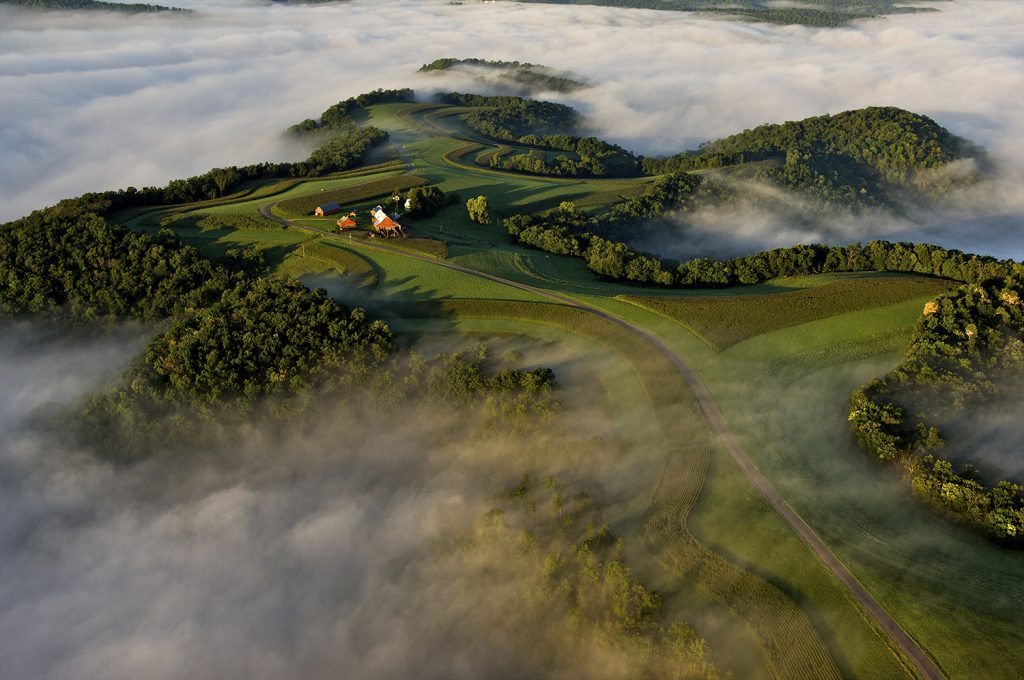 Aerial view of green hills surrounded by fog.