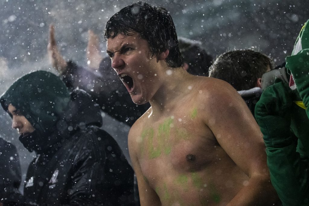 A person with their shirt off screams from the stands of a sports event while it snows outside