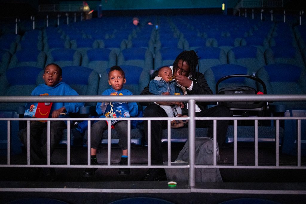 A man feeds a infant in a movie theater while sitting next to two children.