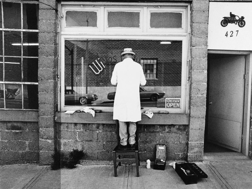 Man standing on a chair painting a store window.
