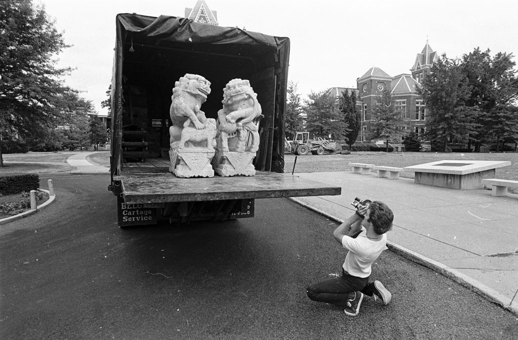Man photographing two statues of Chinese lions on the back of a truck.
