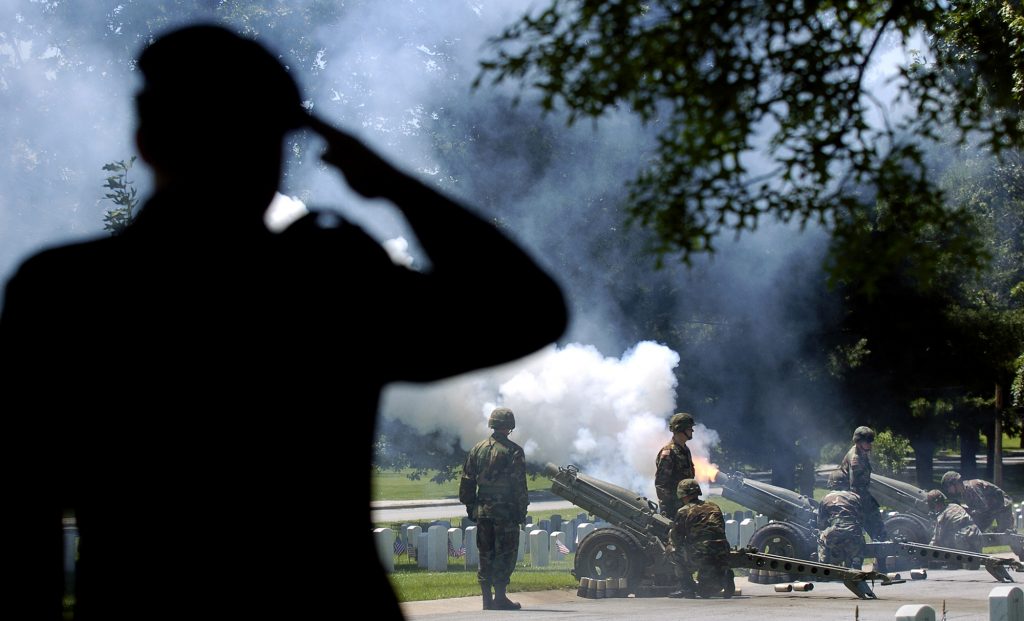 Soldier saluting as other soldiers fire artillery in a Memorial Day ceremony
