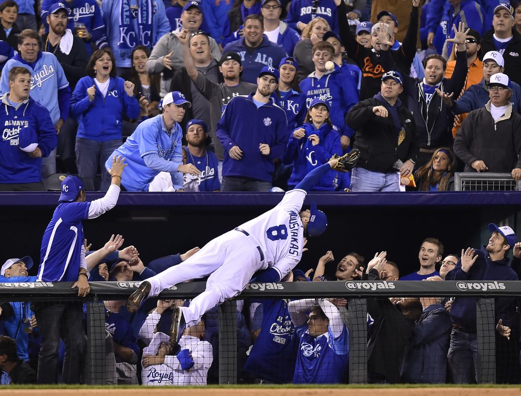 Kansas City Royals baseball player leaning over dugout fence to catch foul ball.