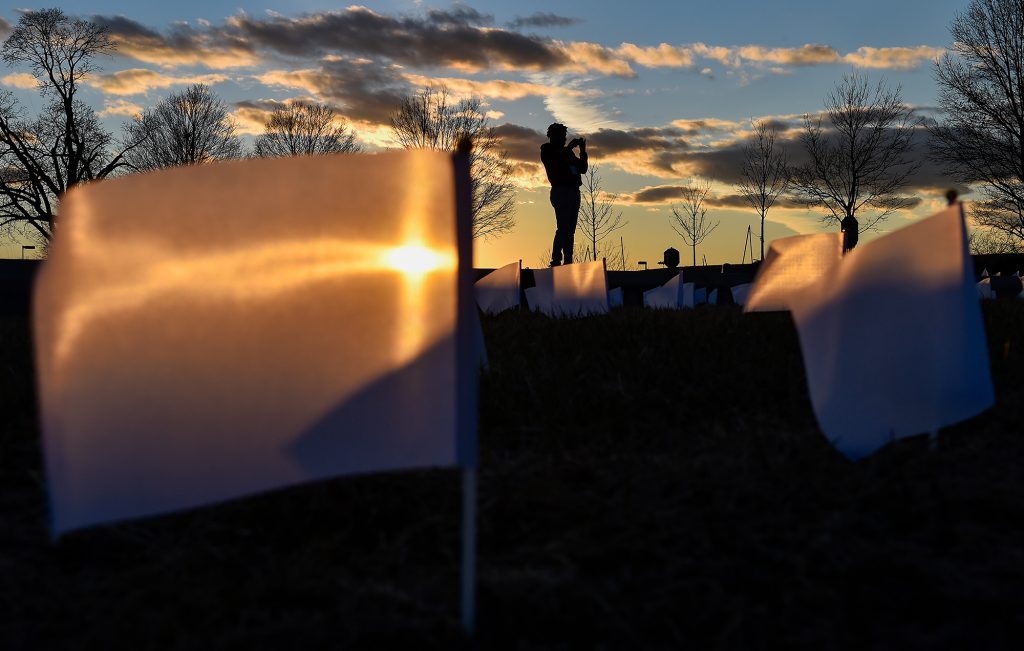 Silhouetted photographer making picture of a memorial sit with white flags at sunset
