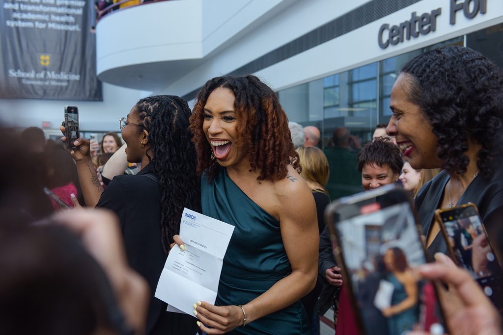 Photograph of excited woman in a crowd holding a piece of paper.