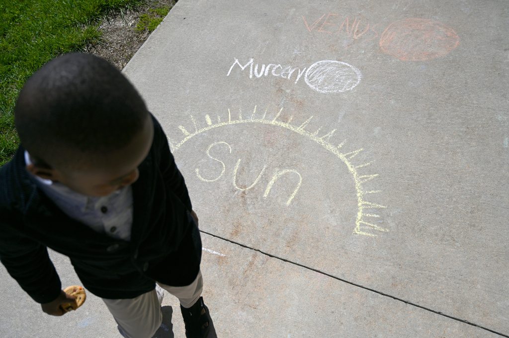 Photograph of a child looking at a sidewalk chalk drawing of the sun and planet