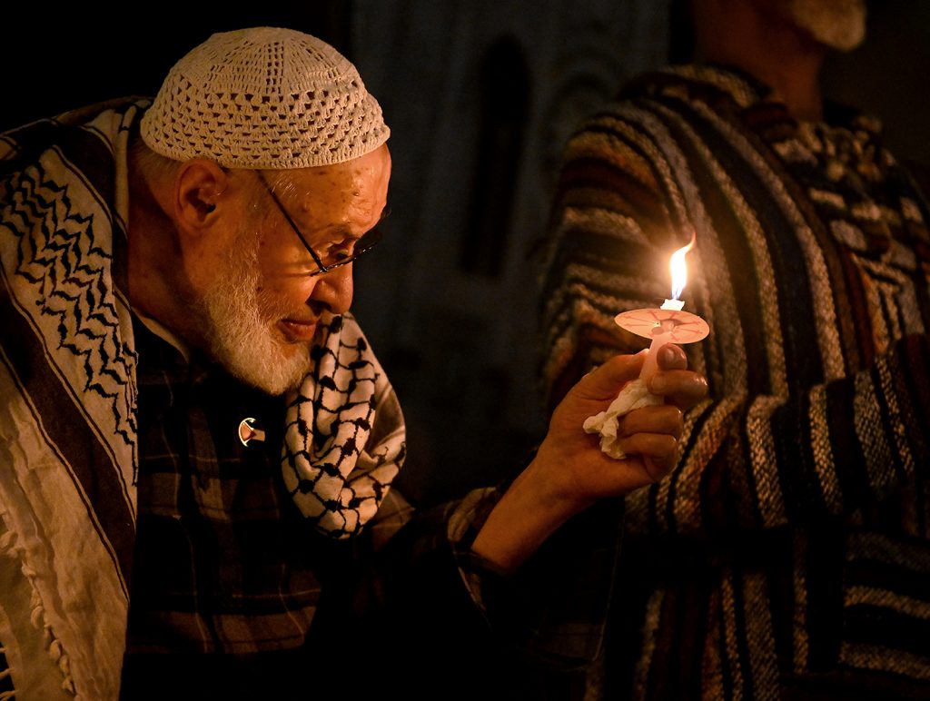 Photograph of an older bearded man holding a candle 