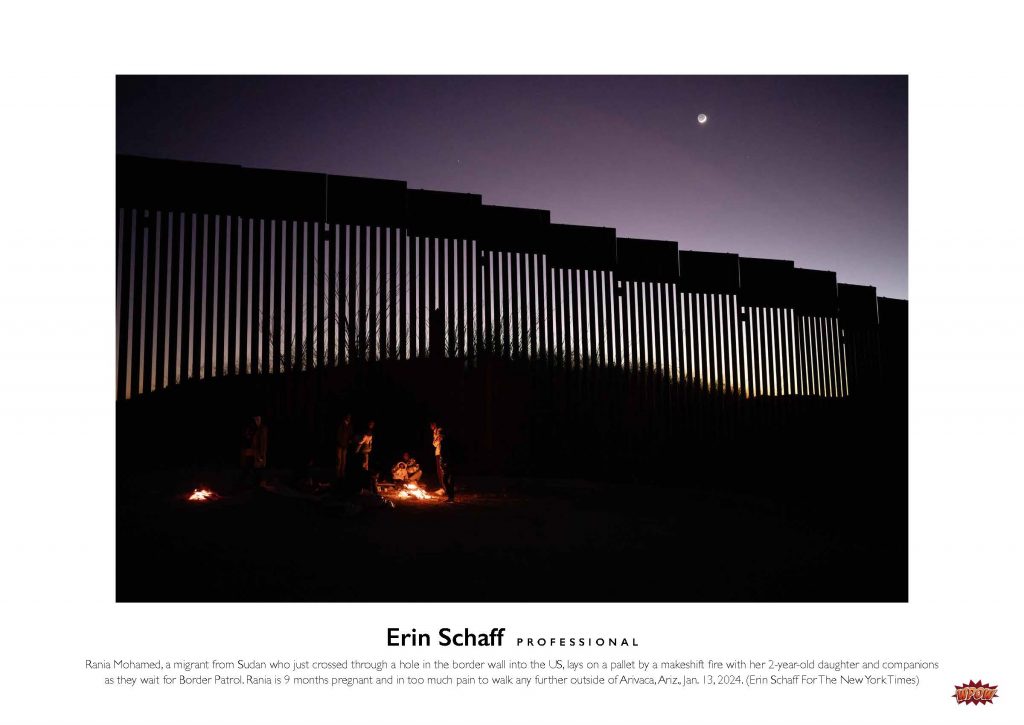 Photograph of a family outside at night around a fire near the US border wall.