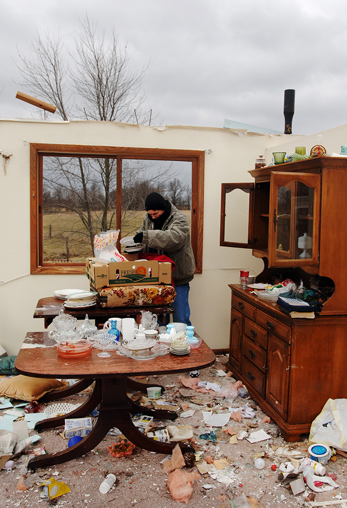 Photograph of a woman sifting through the wreckage of a home after a tornado hit it.