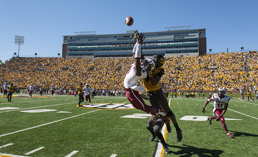 Photograph of football players leaping to catch a pass.
