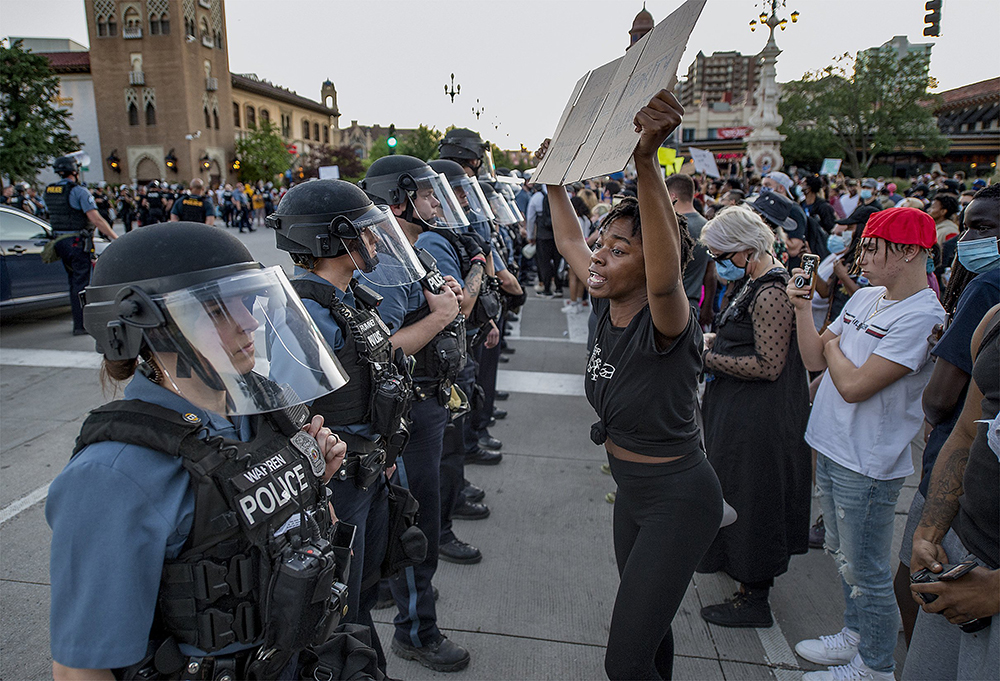 Photograph of a women in front of a crowd confronting police in riot gear during a George Floyd protest in Kansas City.