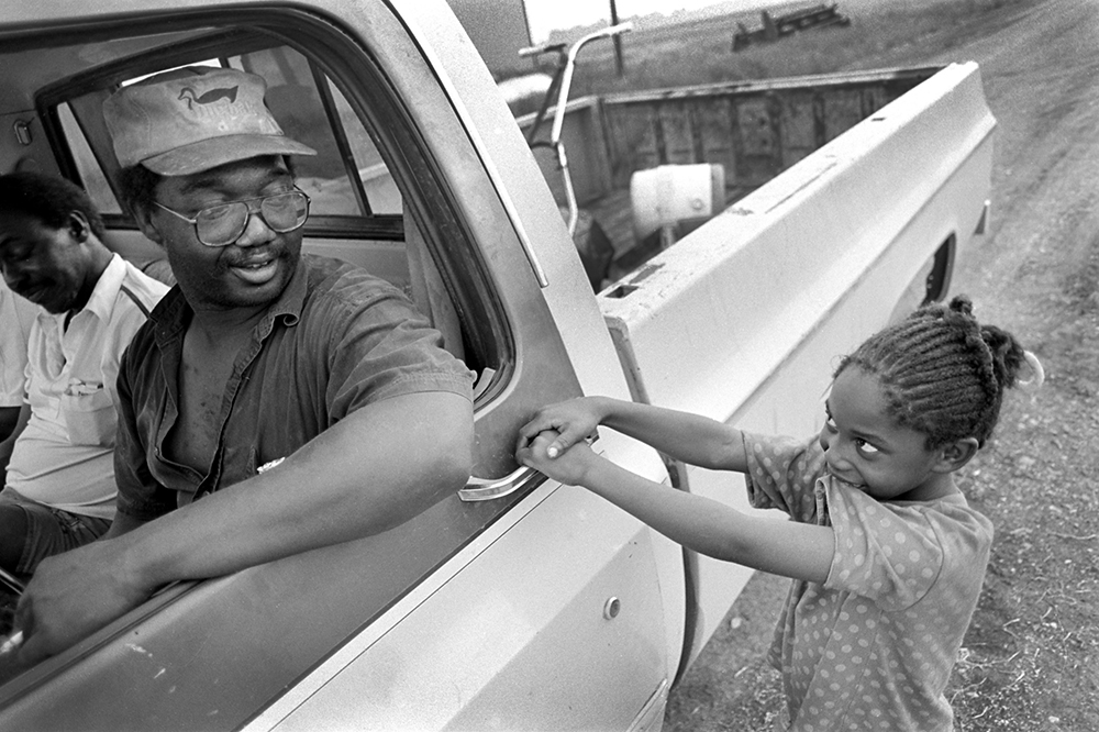 Photograph of a man in a pickup and a girl pulling on the door