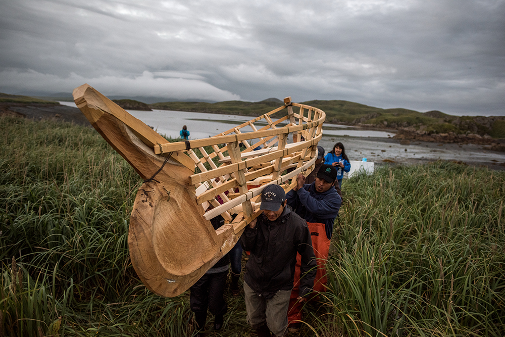 Photograph of a group of people carrying the structure of a small boat.