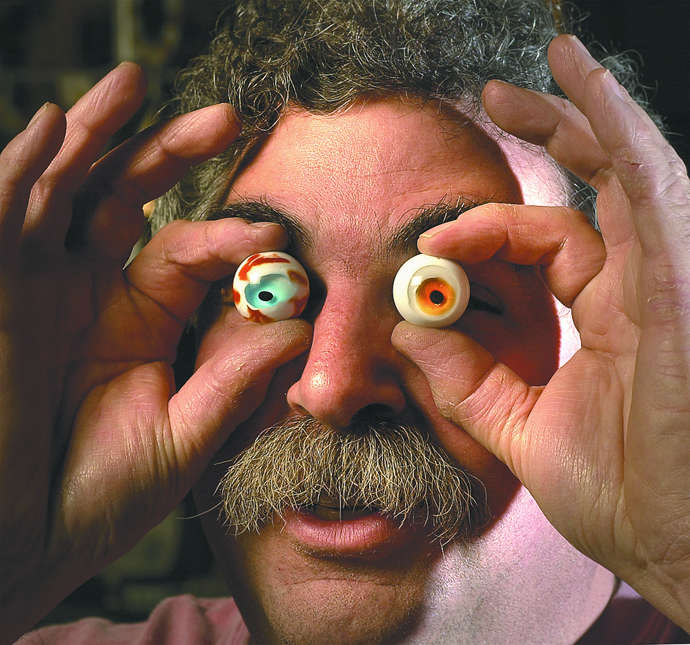 Photograph of a man holding two marbles in front of his eyes.