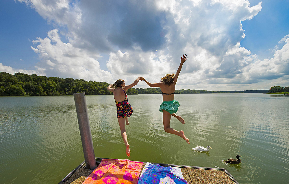 Photograph of two women jumping from a dock into a lake