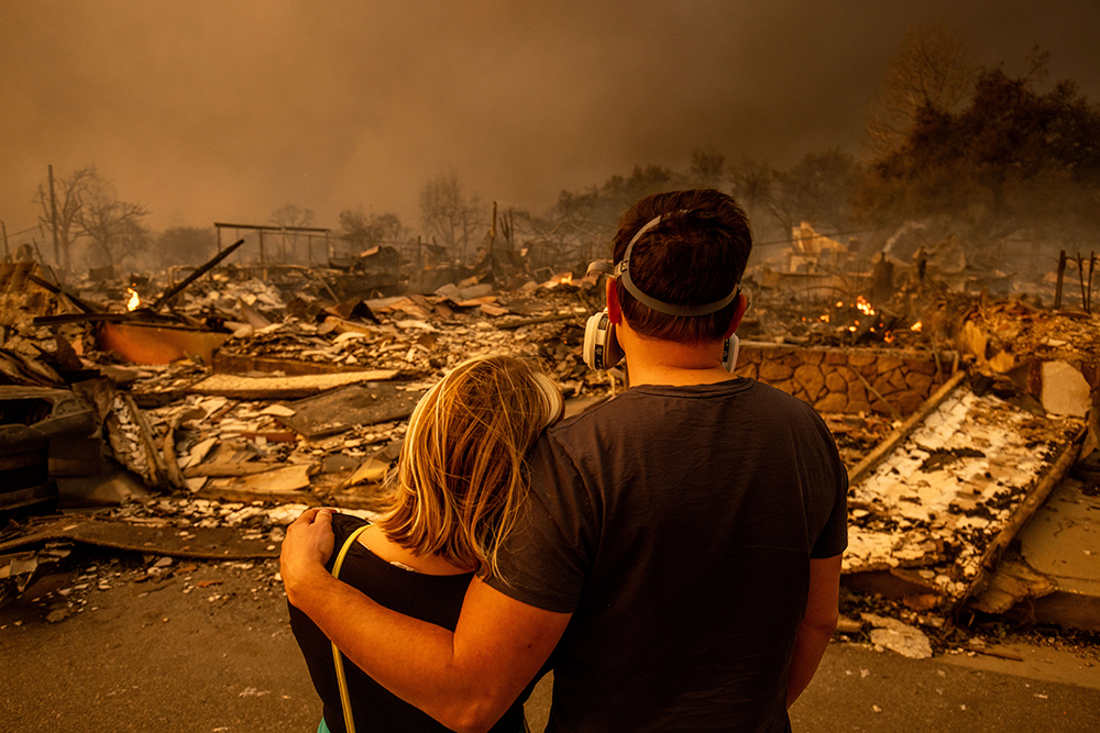 Couple holding each other looking at ruins of burned up home.