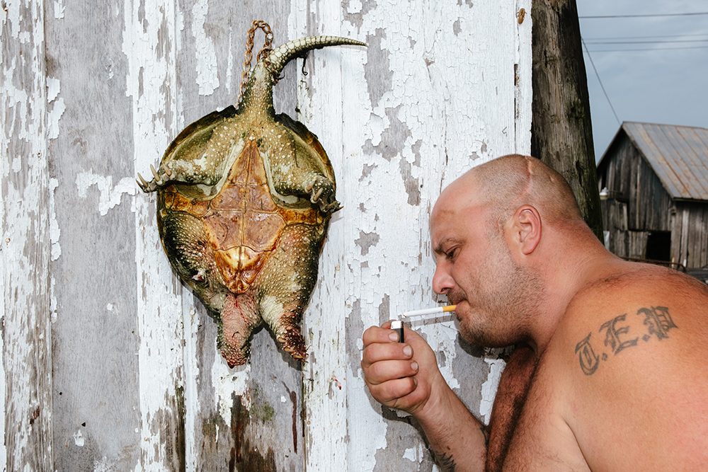 Man lighting a cigarette next to the body of a turtle hanging on a well.